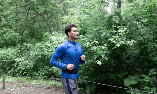 Side view on handsome man in blue sportswear jogging in the wood at the morning time 