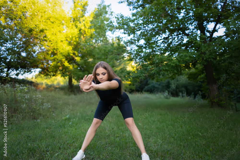 beautiful sports girl in the park is engaged in fitness doing forward bends