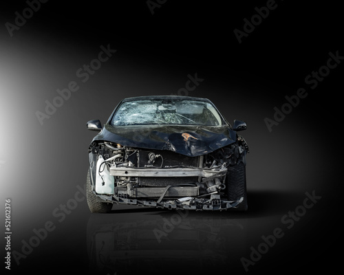 Frontal view of a black crashed car wreck - dented bonnet, smashed engine and broken windshield - in dark studio with copy space