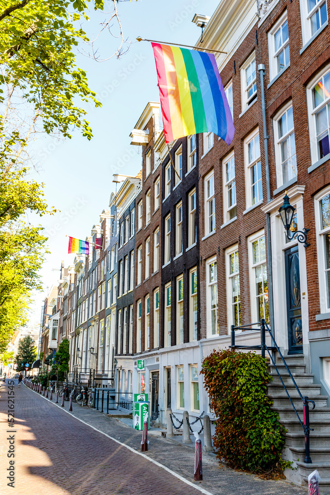 Old Dutch canal houses in Amsterdam with a Progress Pride Flag on their facades during Gay Pride Amsterdam, The Netherlands, Europe