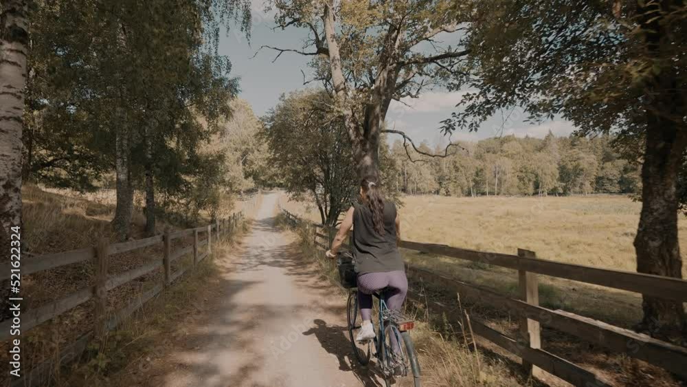 Happy Italian woman riding her bike home through the nature reserve next to wooden fences surrounding the grass pastures. Happy Italian woman riding her bike home through the nature reserve next to wooden fences surrounding the grass pastures.