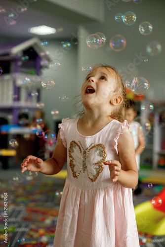 Little girl playing with soap bubbles, dancing, being in a good mood in the playroom. Childhood concept