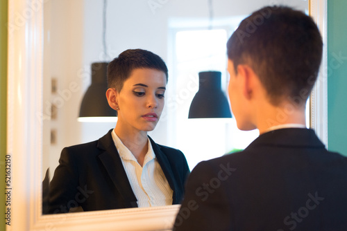 Young businesswoman looking at herself in the mirror at home