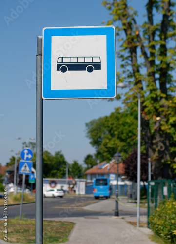 Vertical photo of a Bus stop sign on a metal pole with the street and sky in the background