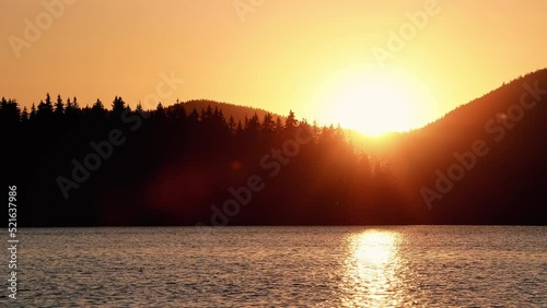 Sunset above mountain range with pine trees. Lake waves in nearground. High contrast, dramatic lighting. Insects, bugs flying