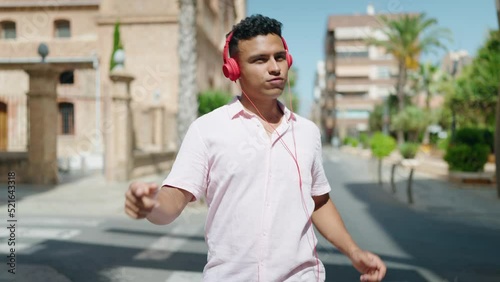Young latin man smiling confident listening to music and dancing at street