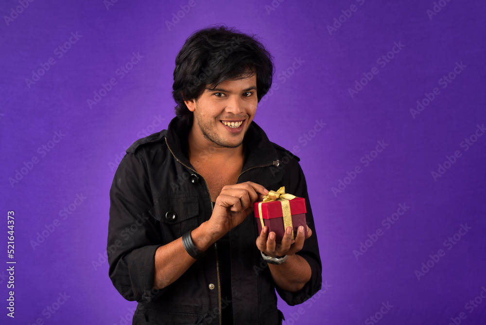 Portrait of young happy smiling handsome man holding gift box on a purple background. Portrait of young happy smiling handsome man holding gift box on a purple background.