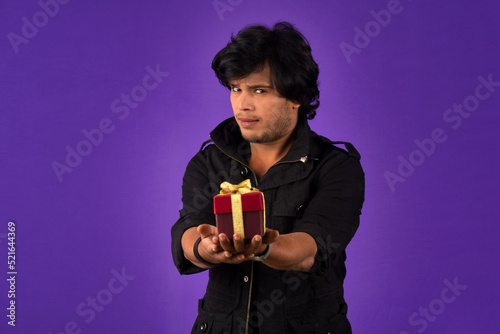 Portrait of young happy smiling handsome man holding gift box on a purple background. © Dip Photography
