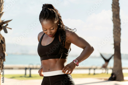 Multiracial woman in sport clothes correcting her sport shorts while standing in front of the sea