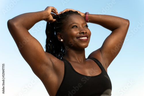 Multiracial woman smiling positively and making ponytail while looking at the distance