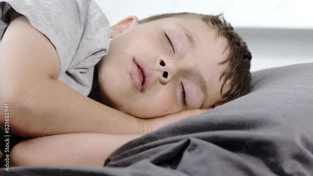 Little preschool boy sleeping in his bed lying on his side. A boy in a gray T-shirt. Little preschool boy sleeping in his bed lying on his side. A boy in a gray T-shirt.