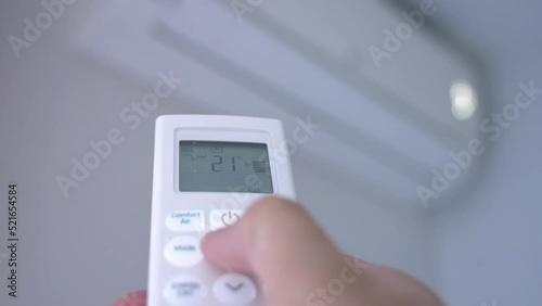 A man's hand pressing the buttons on the control of a split air conditioner to turn it on and set it to the recommended temperature of 25 degrees centigrade photo