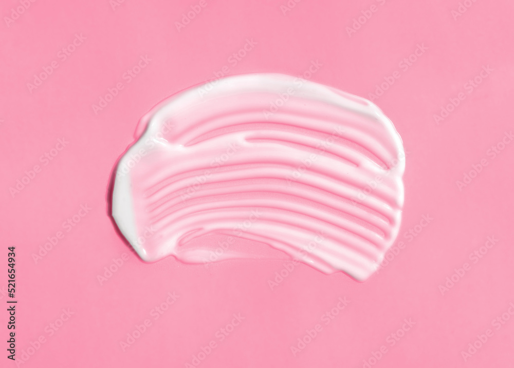 The texture of white cream on pink background. A smear of moisturizer closeup. Lotion swatch. Beauty, skin care product smear smudge drop. SPF sunscreen cream sample