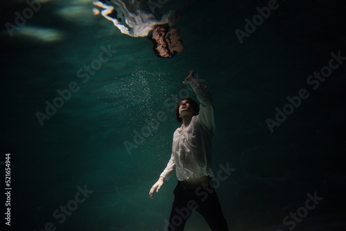underwater shooting with contrasting light  a guy is swimming underwater  pulling his hand to his reflection in the surface of the water. Subconsciousness and self-reflection  concept
