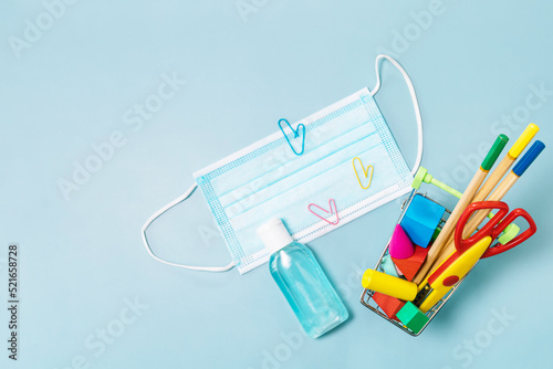 School supplies, poppit anti-stress, face mask, bottle of sanitizer, for back to school on a blue background. Covid-19 precautions, staying healthy. Top view flat lay. Copy space.