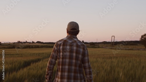 Farmer in front of a sunset agricultural landscape. Man in a countryside field. Country life, food production, farming and country lifestyle concept. © Acronym