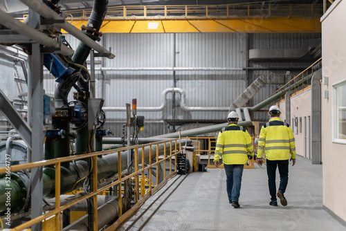 Workers wearing helmets and reflective vests walk the gold mill.