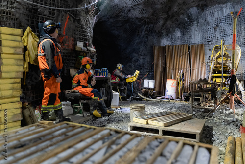 Drillers work in an underground mine on a stationary drilling machine.
