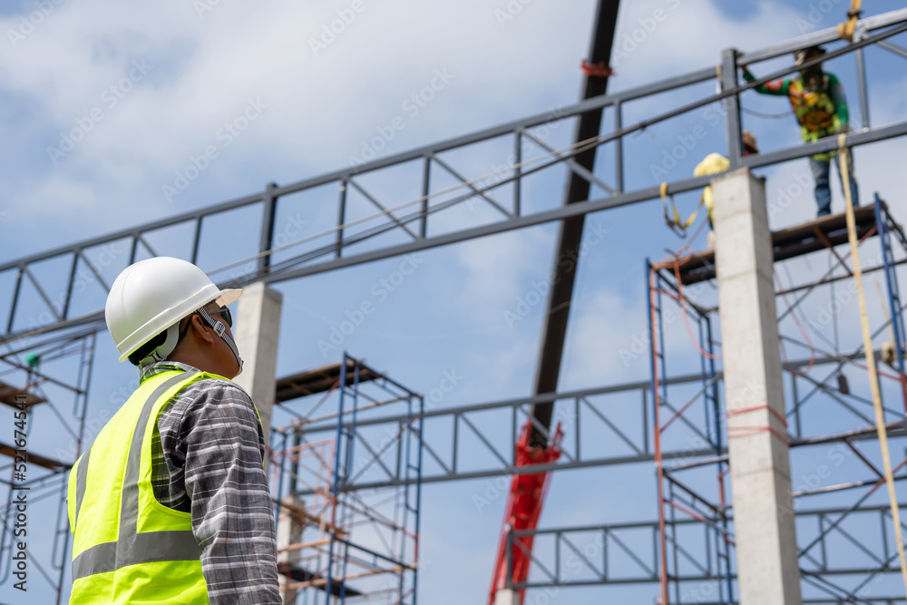 A construction engineer inspects the installation of a factory roof steel frame that uses a mobile crane to lift it up to a height.