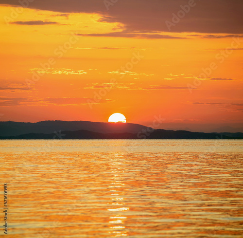 Fototapeta Naklejka Na Ścianę i Meble -  Sunset over Aegean Sea. Greece. Golden reflection on rippled ocean water. Dark land and colorful sky