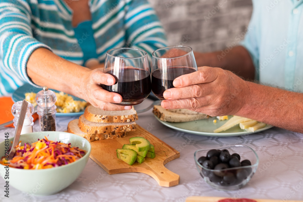 Closeup on caucasian senior couple sitting at the table having brunch at home toasting with glasses of wine Closeup on caucasian senior couple sitting at the table having brunch at home toasting with glasses of wine