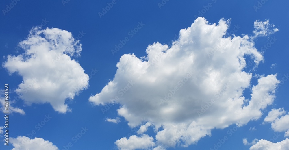 Blue sky with clouds, one bigger and one smaller among other tiny clouds on a bright sunny day