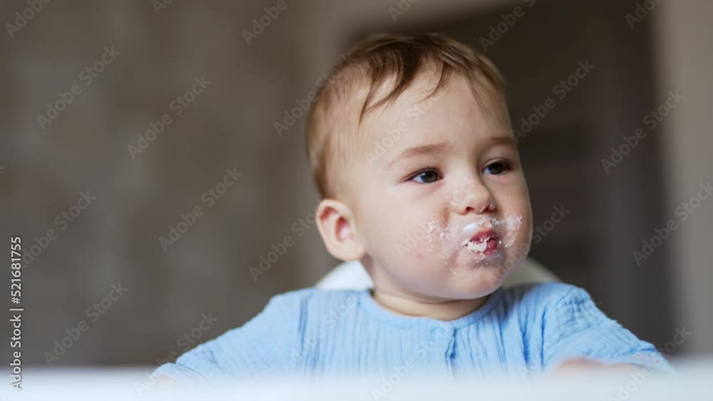 Cute kid eating porridge from spoon. Mother gives porridge to baby and takes the porridge out of kid’s face. Cute kid eating porridge from spoon. Mother gives porridge to baby and takes the porridge out of kid’s face.