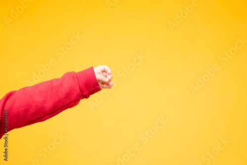 Hand of a little baby isolated in a yellow background. Baby extends her arm and wears a red sweater