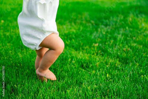 Crop close up of barefoot baby learning to take first steps on lawn