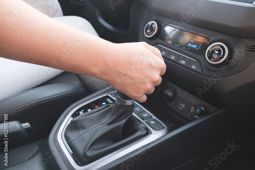 Driver holds on to the shift lever of the automatic transmission. A woman changes gear in a car.