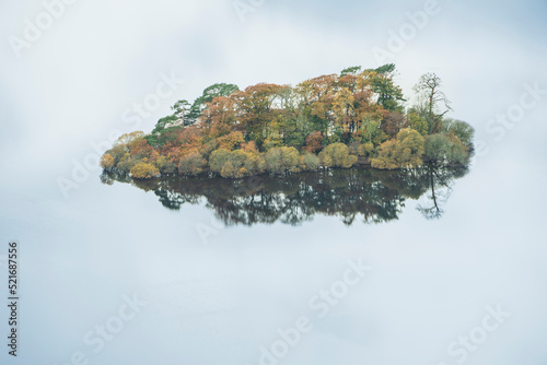 Abstract landscape Autumn image of view of islands in Derwentwater with sky reflections isolating them with deep Fall colors