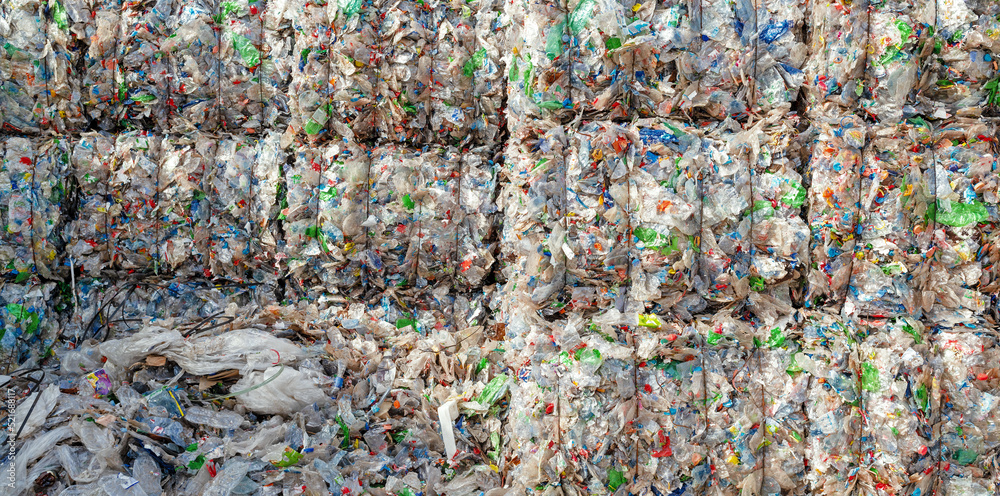 Close-up of a pile of compressed plastic waste in front of a waste recycling plant	