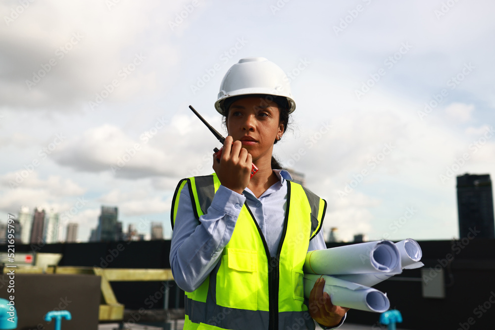 Young female engineer with safety PPE hold drawing and walkie talkie communicate with team Young female engineer with safety PPE hold drawing and walkie talkie communicate with team