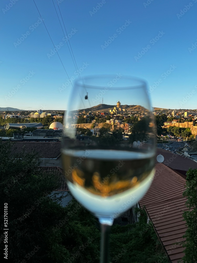 Obraz premium A glass of Georgian wine framing a wonderful cathedral during sunset in Tbilisi, Georgia