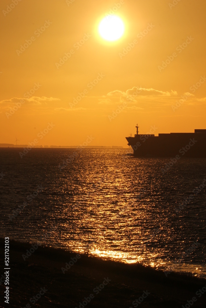 a beautiful sunset at the coast with the sun in an orange sky and the nose of ship in a black sea in summer