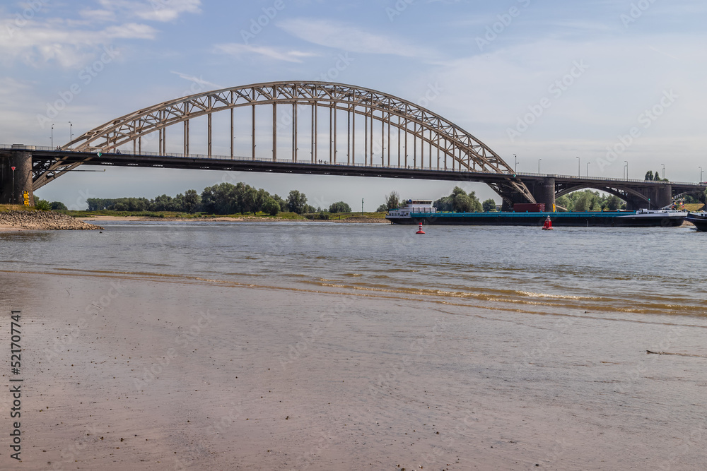 Cargo ship sails under the Waal bridge (Waalbrug) near Nijmegen at very low tide. 