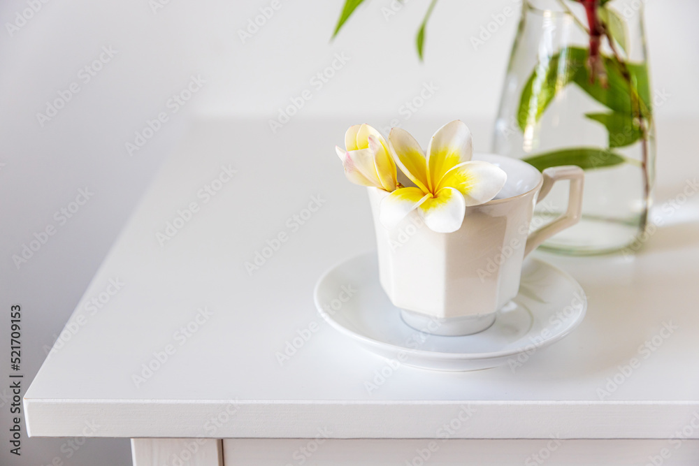 Plumberia rumba in a coffe cup, eucalyptus branch in a vase and cup of coffee on a white table against a wall with two frames. Ready layout. Vertical frame. Space for text