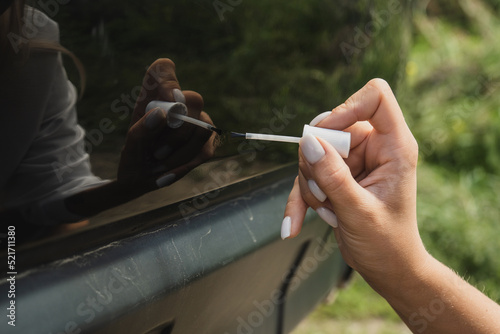 Touching up a body car with a small brush by a young woman