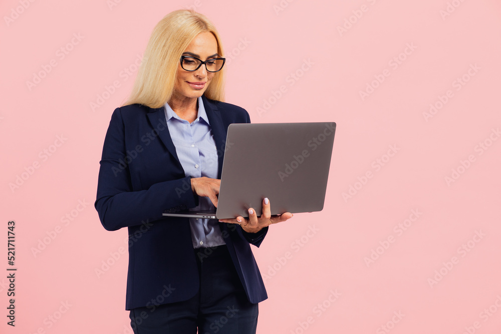 Attractive middle aged business woman in glasses holding a laptop on a pink background Attractive middle aged business woman in glasses holding a laptop on a pink background