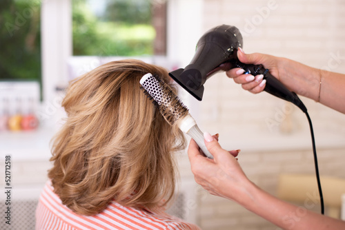  Female hairdresser's hand brushing and blow drying blonde hair in beauty salon