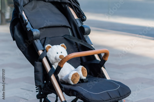 Soft toy teddy bear sitting in a baby stroller on blurred background of city street