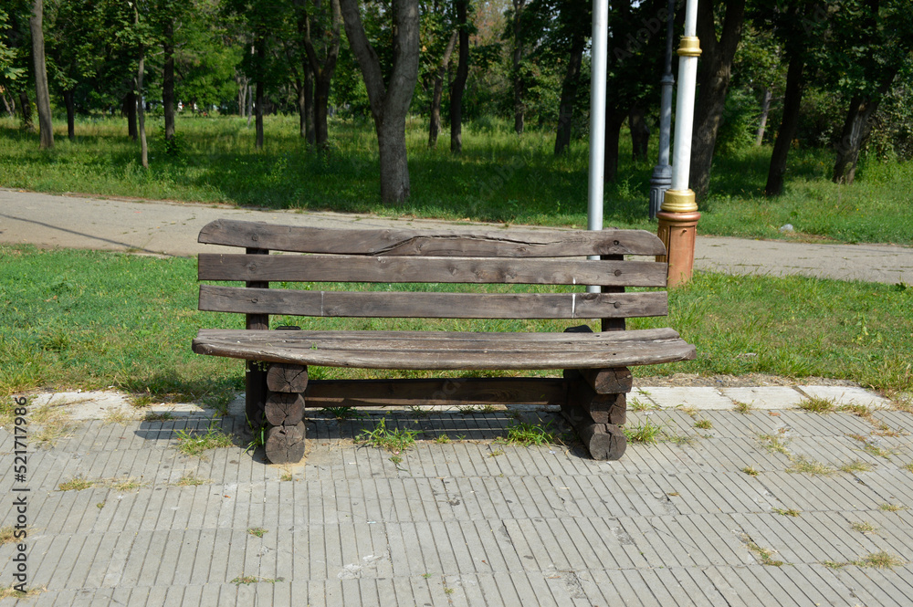 Empty old wooden bench in a sunny garden or park area, outdoors. the tree has darkened and cracked from the weather Empty old wooden bench in a sunny garden or park area, outdoors. the tree has darkened and cracked from the weather