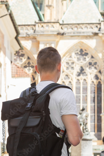 Rear view of young man in white t-shirt with big black backpack exploring streets of Prague old town, Czech Republic.