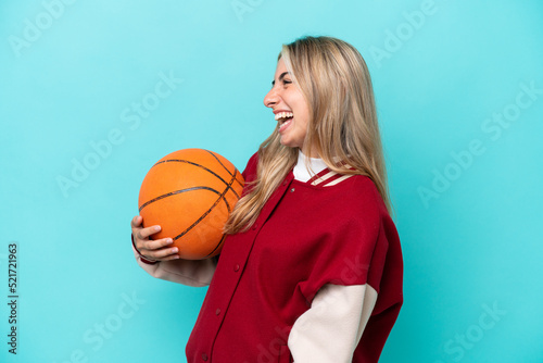 Young caucasian basketball player woman isolated on blue background laughing in lateral position