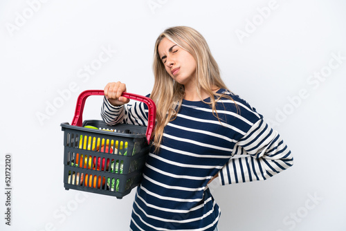 Young caucasian woman holding a shopping basket full of food isolated on white background suffering from backache for having made an effort