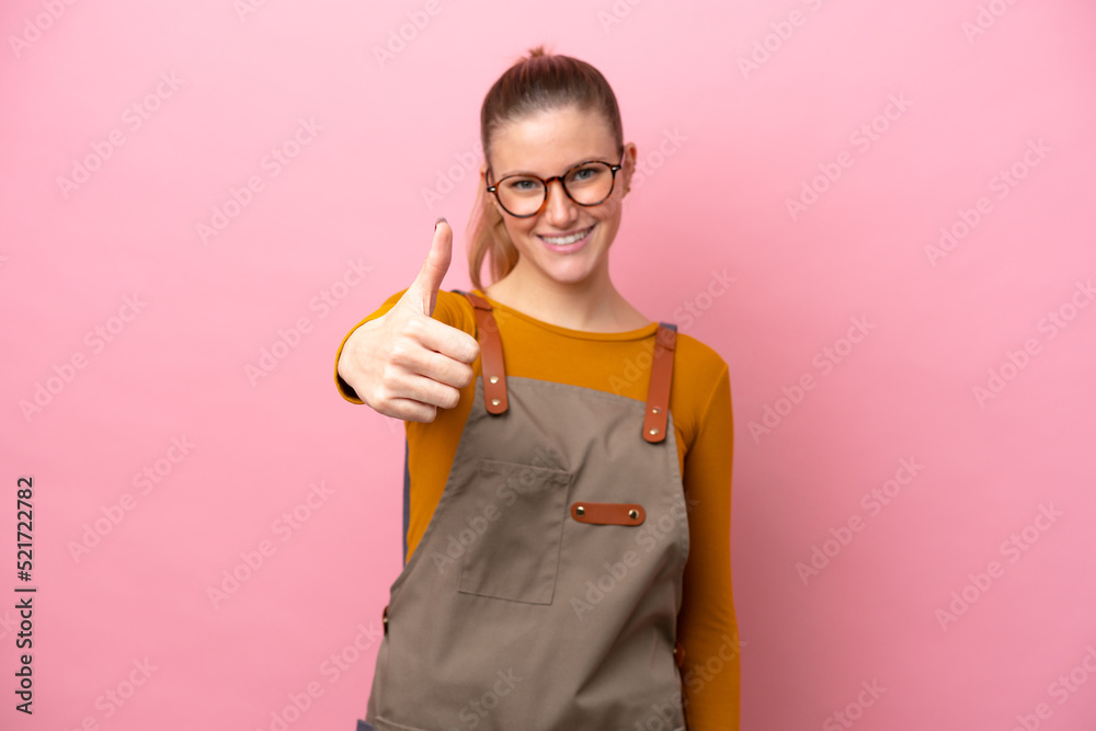 Woman with apron isolated on pink background with thumbs up because something good has happened Woman with apron isolated on pink background with thumbs up because something good has happened