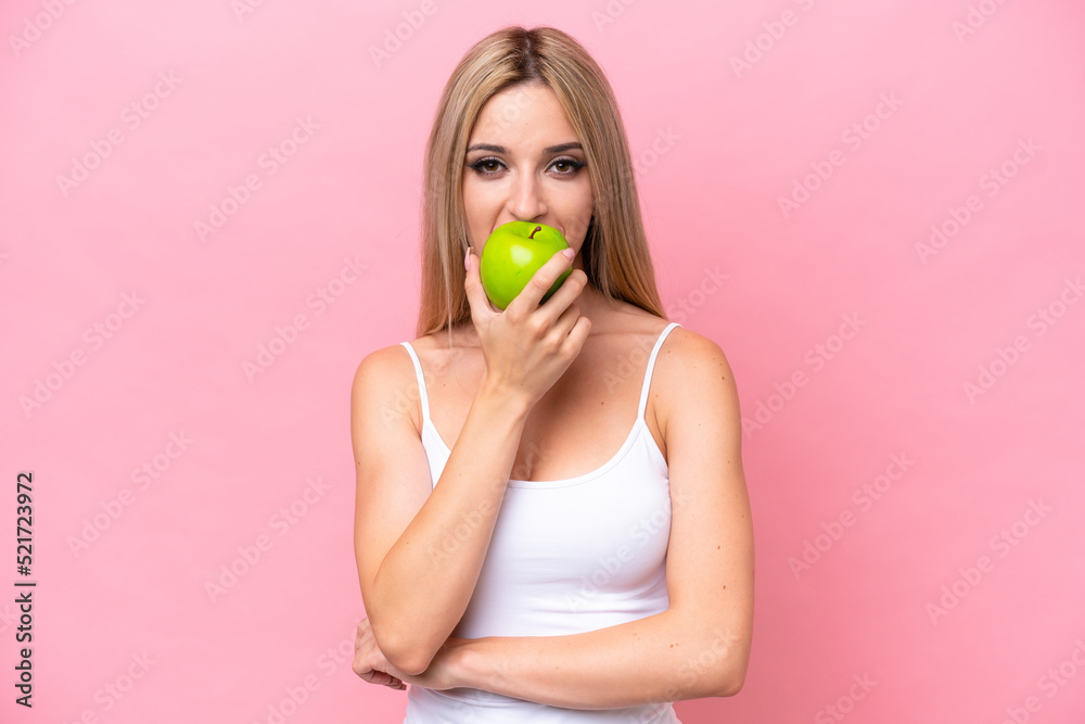 Pretty blonde woman isolated on pink background eating an apple Pretty blonde woman isolated on pink background eating an apple