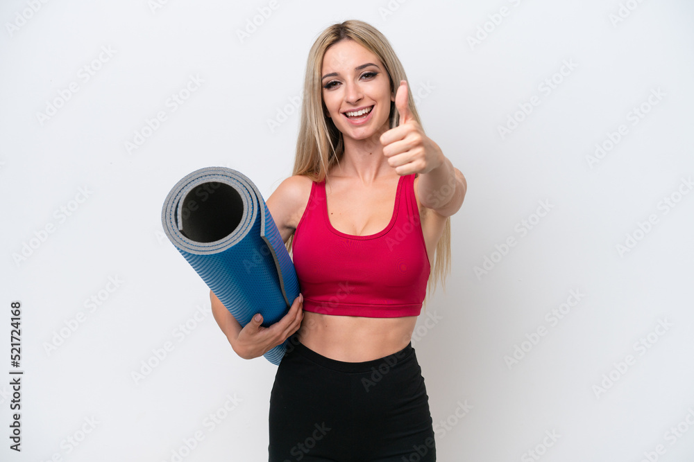 Young sport blonde woman going to yoga classes while holding a mat isolated on white background with thumbs up because something good has happened