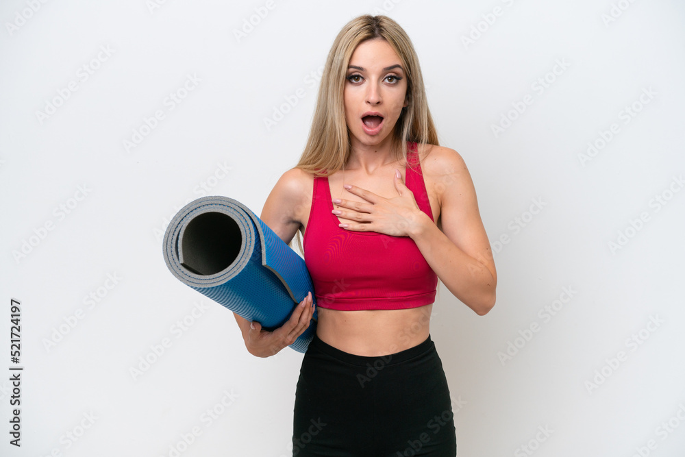 Young sport blonde woman going to yoga classes while holding a mat isolated on white background surprised and shocked while looking right Young sport blonde woman going to yoga classes while holding a mat isolated on white background surprised and shocked while looking right