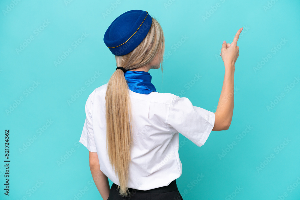 Airplane blonde stewardess woman isolated on blue background pointing back with the index finger Airplane blonde stewardess woman isolated on blue background pointing back with the index finger